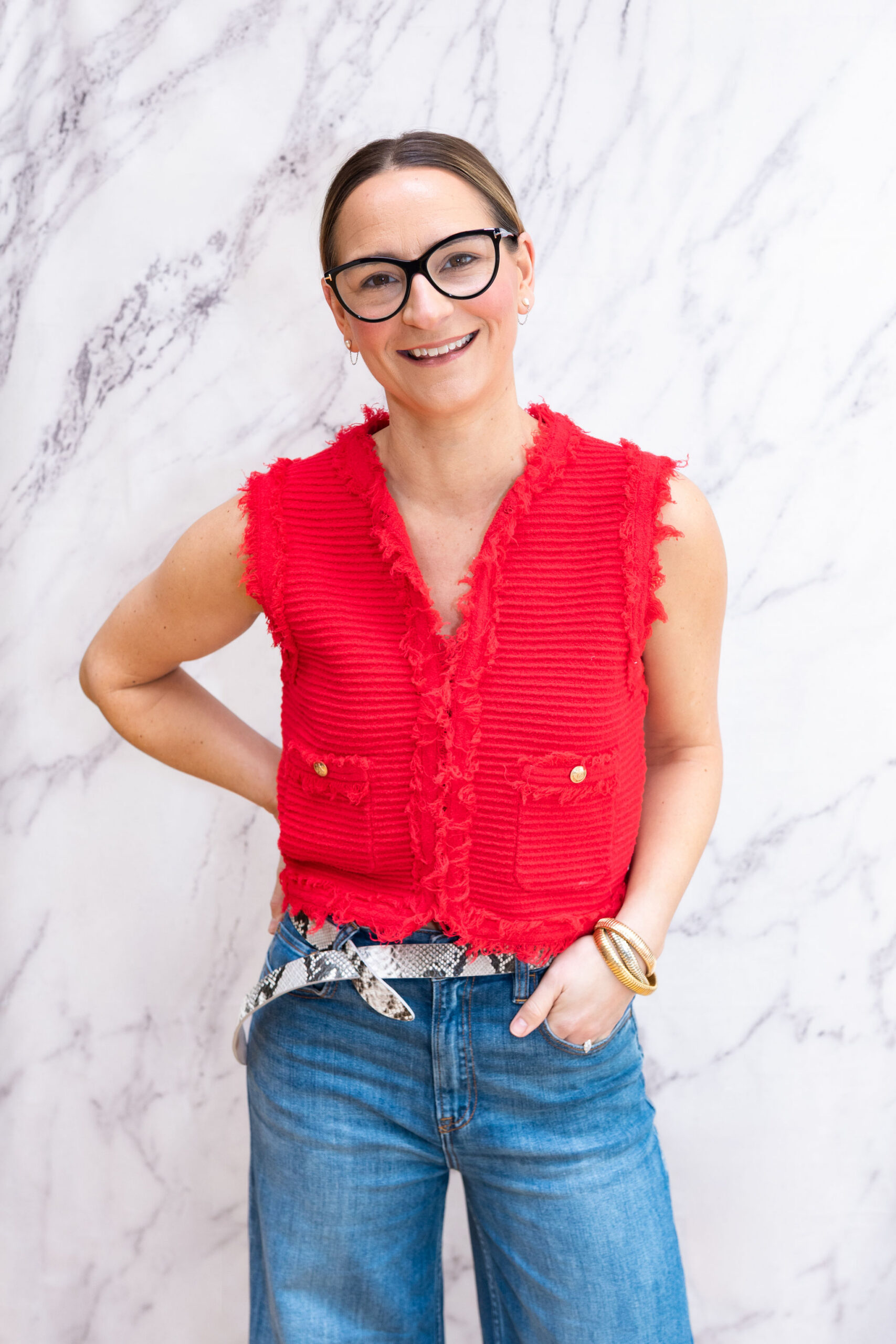 woman smiling at camera wearing red shirt vest and glasses and denim jeans