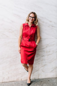 woman smiling wearing a red trench dress leaning against a white marble wall